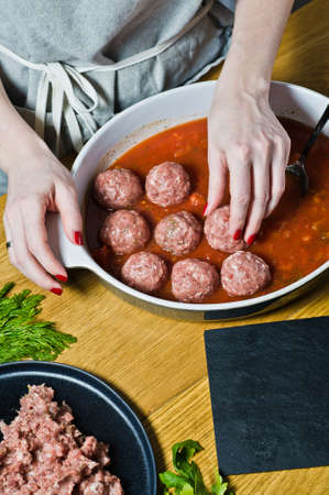 The chef prepares Italian meatballs from raw minced meat, puts in a baking dish with tomato sauce. Black background, top view, kitchenの写真素材