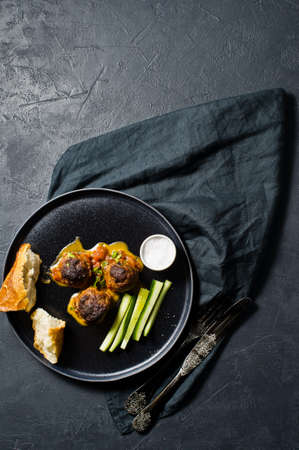 Meat balls in tomato sauce on a black plate, cucumbers, salt, bread. Black background, top view,...