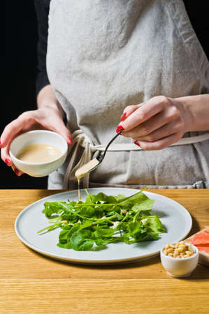 The chef lays out the arugula leaves on a plate, cooked. Black background, side view, kitchenの写真素材