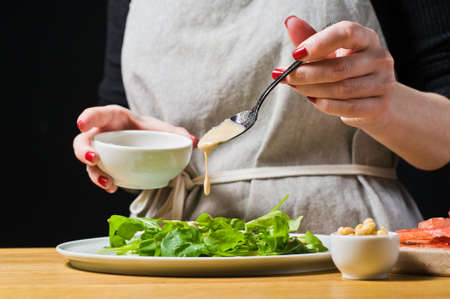 The chef lays out the arugula leaves on a plate, cooked. Black background, side view, kitchenの写真素材