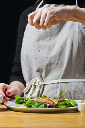 The chef squeezes grapefruit juice on a plate of salad. Black background, side view, kitchenの写真素材