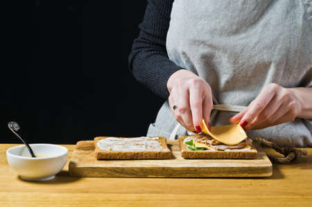 The chef prepares a sandwich, puts slices of cheese on toast. Black background, side view, kitchenの写真素材