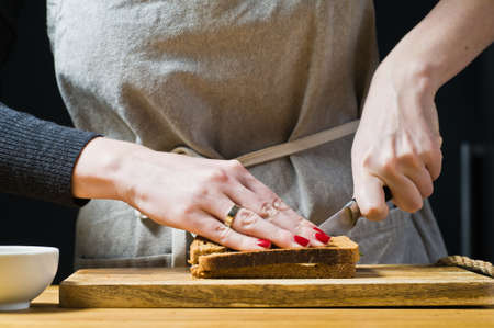 The chef prepares a sandwich of toast black bread. Black background, side view, kitchen