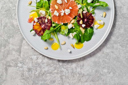 Salad with arugula, grapefruit, red oranges, nuts and cheese. Gray background, top view, space for textの写真素材