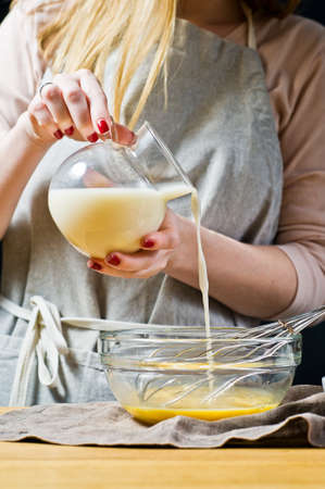 Chef pouring oat milk in a bowl. The concept of cooking gluten-free and lactose-free baking. Ingredients: quail eggs, sugar, gluten-free flour, oat milk. Black background, side view, kitchenの写真素材