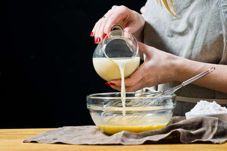 Chef pouring oat milk in a bowl. The concept of cooking gluten-free and lactose-free baking. Ingredients: quail eggs, sugar, gluten-free flour, oat milk. Black background, side view, kitchenの写真素材