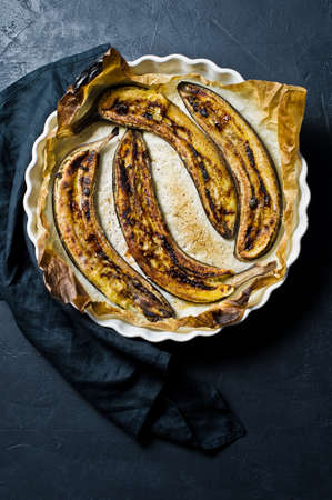 Baked bananas with honey in a baking dish. Black background, top view, space for textの写真素材