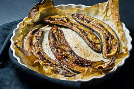 Fried bananas with honey in a baking dish. Black background, top viewの写真素材