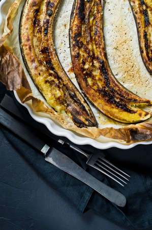 Fried bananas with honey in a baking dish. Black background, top view, space for text