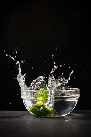 Broccoli with splashes falls in a bowl of water. Black background, view C, space for textの写真素材