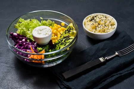 Salad bowl, healthy and balanced food. Ingredients broccoli, corn, carrots, couscous, lettuce, cabbage, sauce. Black background, side view, space for textの写真素材