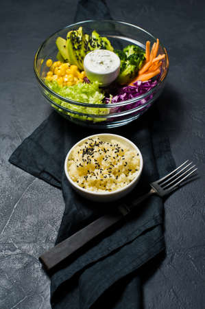 Salad bowl, healthy vegetarian food. Ingredients broccoli, corn, carrots, couscous, lettuce, cabbage, sauce. Black background, side viewの写真素材