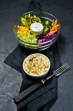 Salad bowl, healthy and balanced food. Ingredients broccoli, corn, carrots, couscous, lettuce, cabbage, sauce. Black background, side view, space for textの写真素材