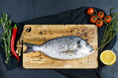 Dorado fish raw on a wooden chopping Board, ingredient rosemary, tomatoes, chili, lemon, thyme,...