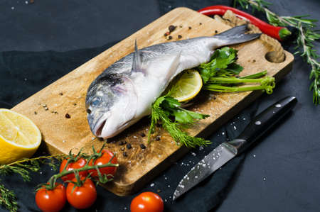 Stuffed Dorado fish on a wooden chopping Board. Ingredient rosemary, tomatoes, chili, lemon, thyme,...