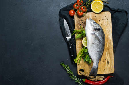 Stuffed Dorado fish on a wooden chopping Board. Ingredient rosemary, tomatoes, chili, lemon, thyme,...
