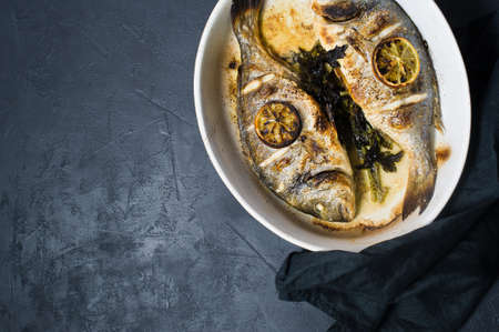 Baked Dorado fish with a slice of lemon. Dark background, top view, space for textの写真素材