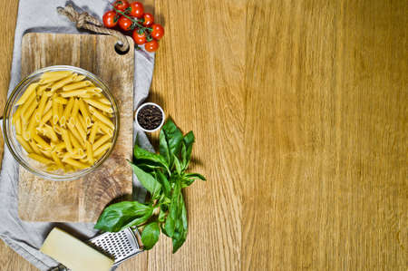 Pasta Penne, ingredients for cooking. Cherry tomatoes, Basil, Parmesan, pepper. Wooden background,...