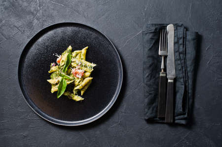 Italian pasta Penne with spinach, cherry tomatoes and Basil. Black background, top view, close up