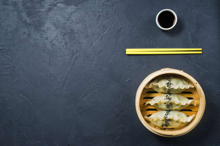Japanese gyoza in a traditional steamer, yellow chopsticks. Dark background, top view, space for textの写真素材
