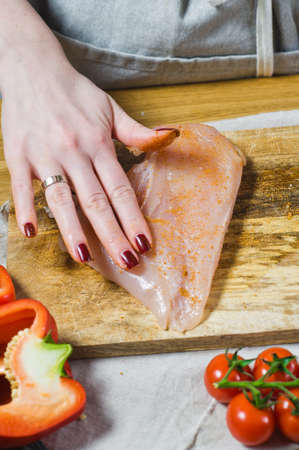The chef marinates chicken Breasts in paprika on a wooden cutting Board. Background kitchen, side viewの写真素材