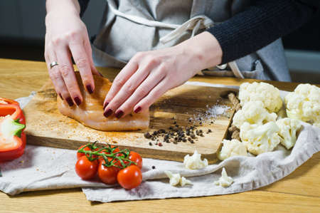The chef marinates chicken Breasts in paprika on a wooden cutting Board. Background kitchen, side viewの写真素材