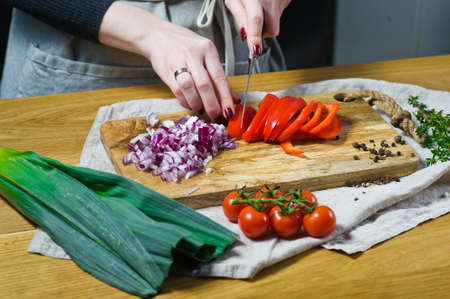 The chef cuts red bell peppers on a wooden chopping Board. Background kitchen, side view