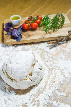 Ingredients for Focaccia: dough, tomatoes, rosemary, thyme, Basil, olive oil on a wooden table. Side...