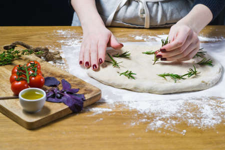The chef prepares Focaccia, lays rosemary on the dough. Top view, wooden background