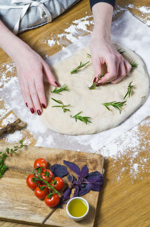 The chef prepares Focaccia, lays rosemary on the dough. Top view, wooden backgroundの写真素材