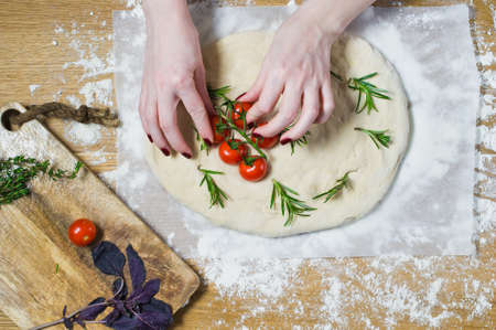 The chef prepares Focaccia, lays tomatoes on the dough. Top view, wooden background