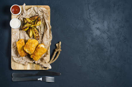 English traditional fish and chips on a wooden chopping Board. Dark background, top view, space for...