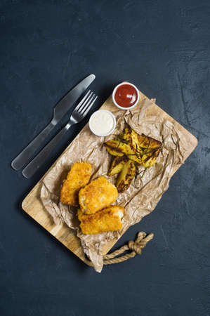 English traditional fish and chips on a wooden chopping Board. Dark background, top viewの写真素材