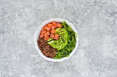 Poke bowl. Ingredients: salmon, avocado, brown rice, seaweed. Gray background, top view, space for...