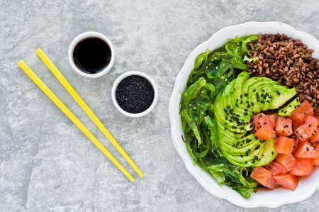 Salmon salad, avocado, brown rice, seaweed. Gray background, side view, space for text
