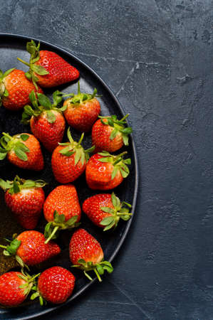 Strawberries on a black plate. Black background, top view, space for textの写真素材