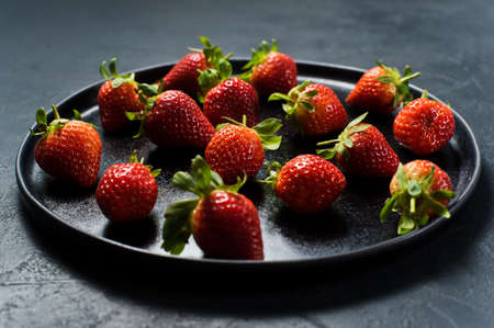 Strawberries on a black plate. Black background, side view, space for textの写真素材