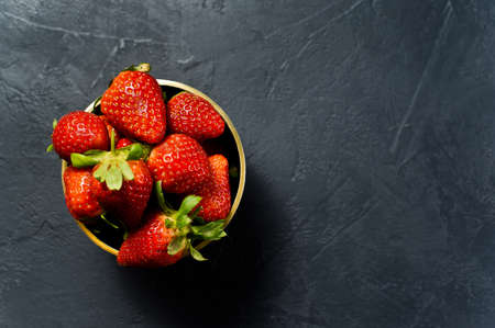 Ripe strawberries in a Golden bowl. Black background, top view, space for textの写真素材