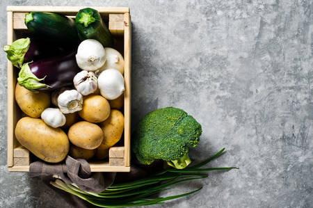 Vegetables in a wooden box: potatoes, onions, garlic, eggplant, zucchini, broccoli, green onions....