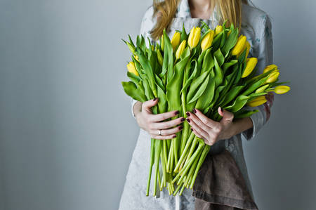 Girl florist holding a bunch of yellow tulips. Floristic. Gray backgroundの写真素材
