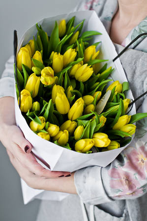 Girl holding a bunch of yellow tulips. Floristic. Gray backgroundの写真素材