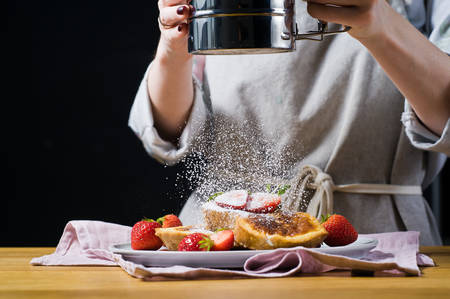 The hands of the chef, sprinkle with powdered sugar French toast. Black background, side view, space for text, kitchenの写真素材
