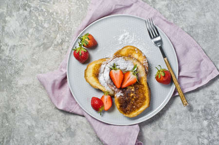 French toast with strawberries and maple syrup on a gray plate. Gray background, top view, space for...