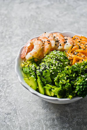 Buddha bowl with shrimps, avocado, carrot, brocoli and rice. Gray background, side view, space for textの写真素材