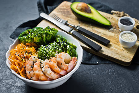 The Buddha bowl a balanced healthy meal. Ingredients: shrimps, avacado, carrots, broccoli and rice. Black background, side viewの写真素材