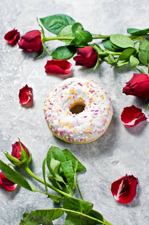 White doughnuts with sprinkles, decorated with a red rose. Gray background, top viewの写真素材