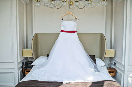 White wedding dress of the bride hanging on the chandelier in the hotel roomの写真素材