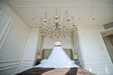 White wedding dress of the bride hanging on the chandelier in the hotel roomの写真素材