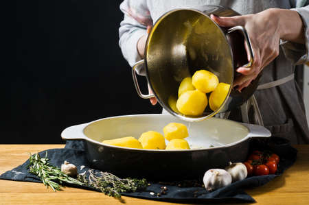 Chef pours potatoes in a baking dish. The concept of cooking baked potatoes. Black background, side view, space for text, kitchenの写真素材