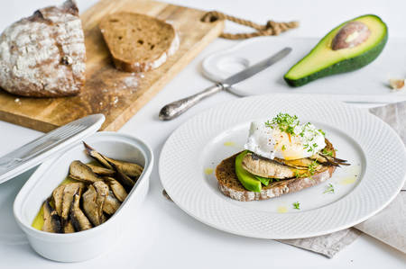 Black bread sandwich with avocado, poached egg and sprats. White background, side view